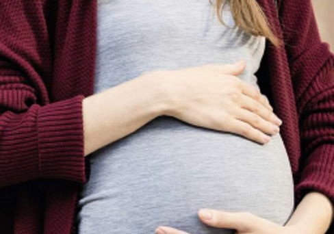 Close up Junge Schwangere Frau haelt mit beiden Haenden ihren Bauch in huebscher Umstandsmode