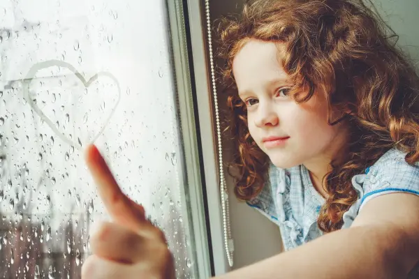 Glückliches Mädchen malt Herz an Fensterscheibe